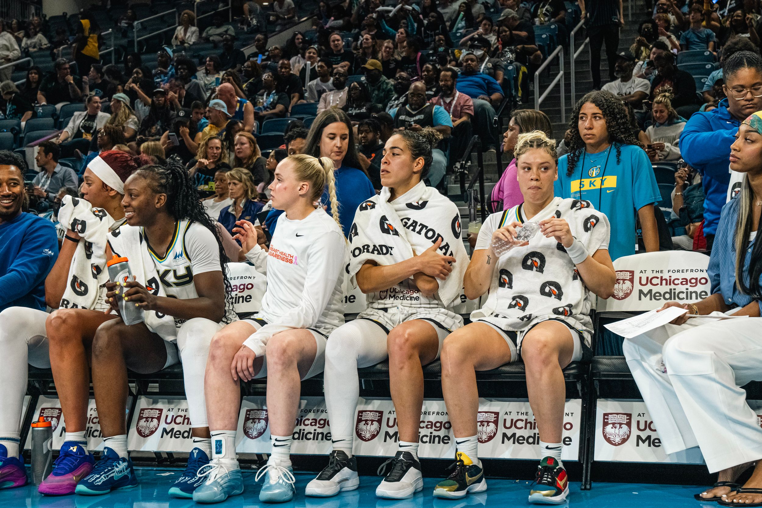 Row of basketball players in white uniforms sitting together on the team bench during a game.