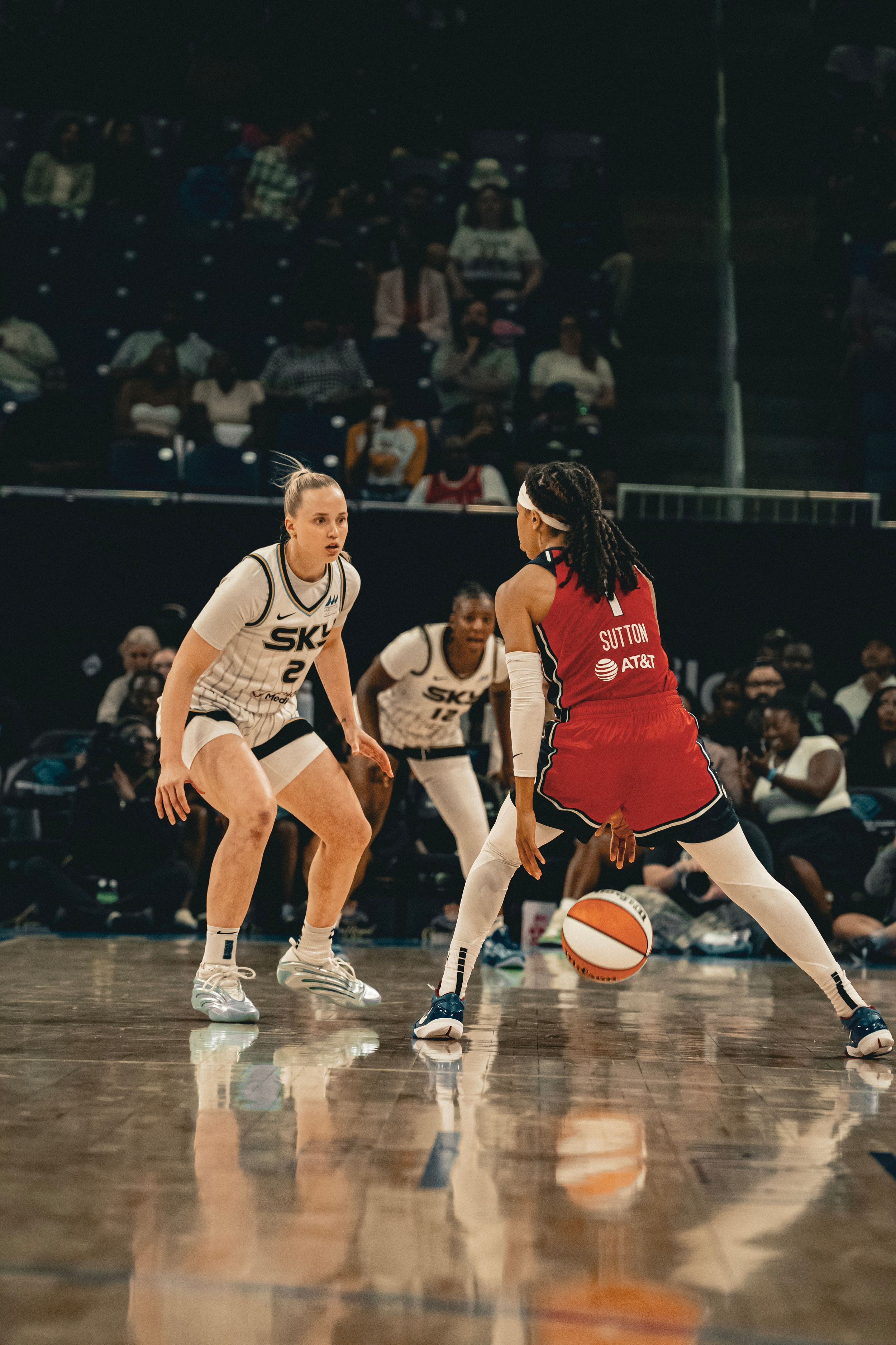 Two professional basketball players face off during a competitive WNBA game on a glossy court.