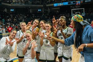Basketball team members celebrate together on the court wearing matching white striped uniforms.