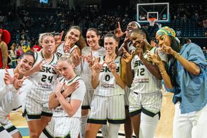 Basketball players wearing white striped uniforms celebrate together on the court after an exciting game.