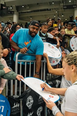 Athletes signing autographs for eager fans behind barriers at a sporting event.