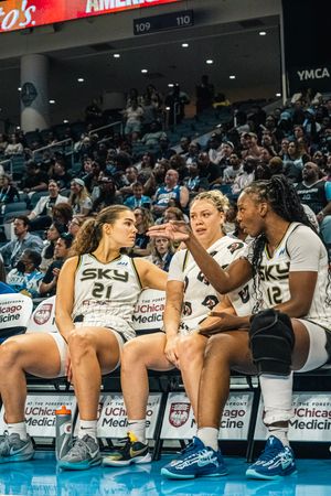 Basketball team members in Sky jerseys rest together on the sideline during a match.