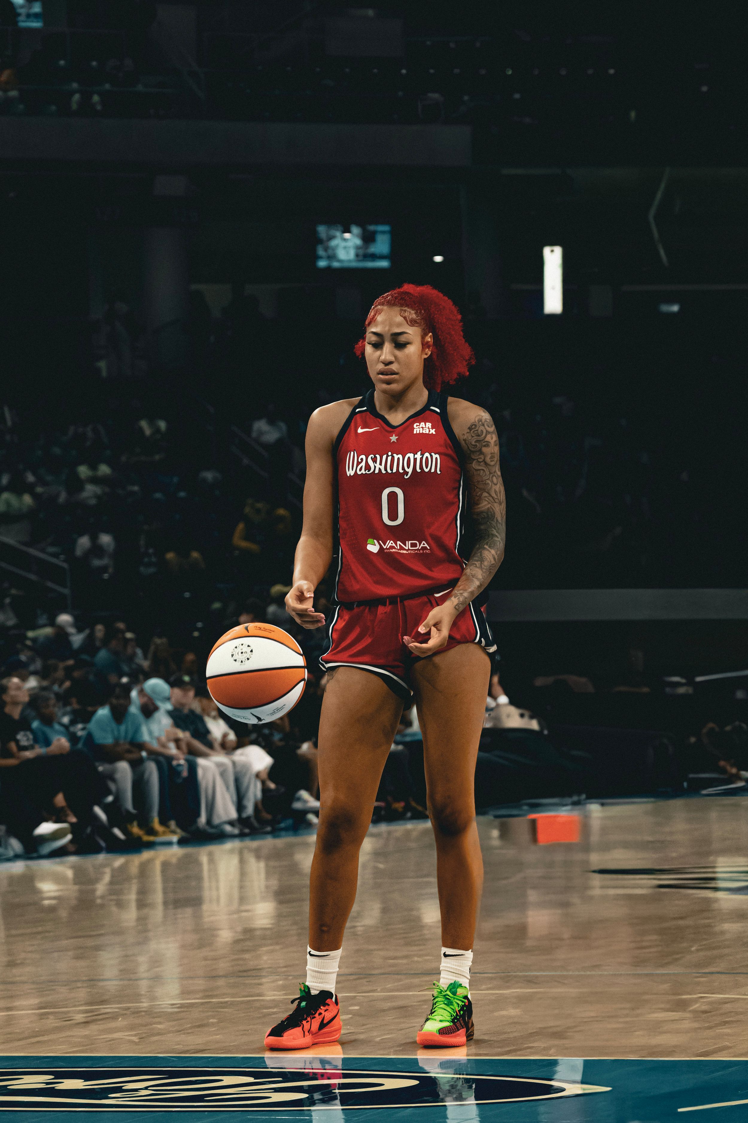 WNBA player in red Washington Mystics jersey number 0 dribbles basketball during professional game on court.