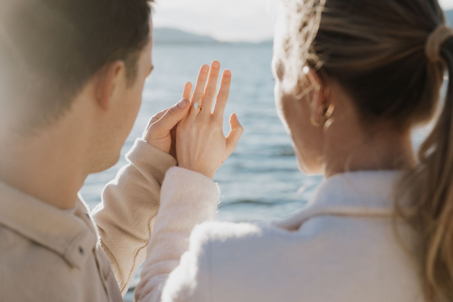 A romantic beach proposal scene at sunset with one person kneeling on the shoreline in front of another.