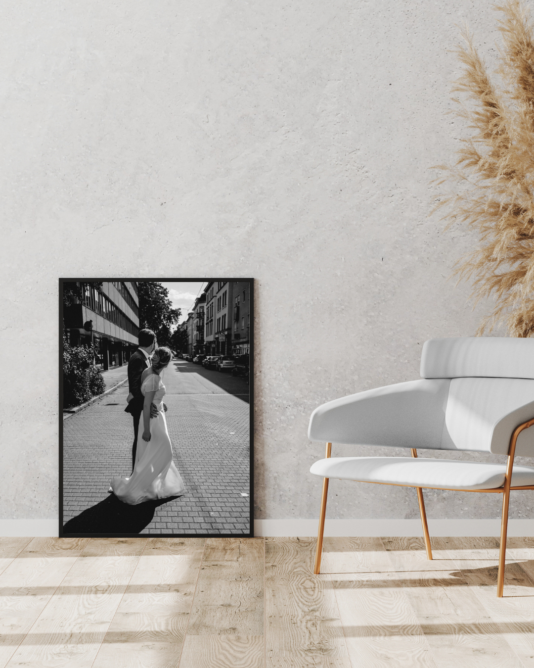 Modern wedding photography display on white wall with plush chairs and dried pampas grass creating minimalist decor.