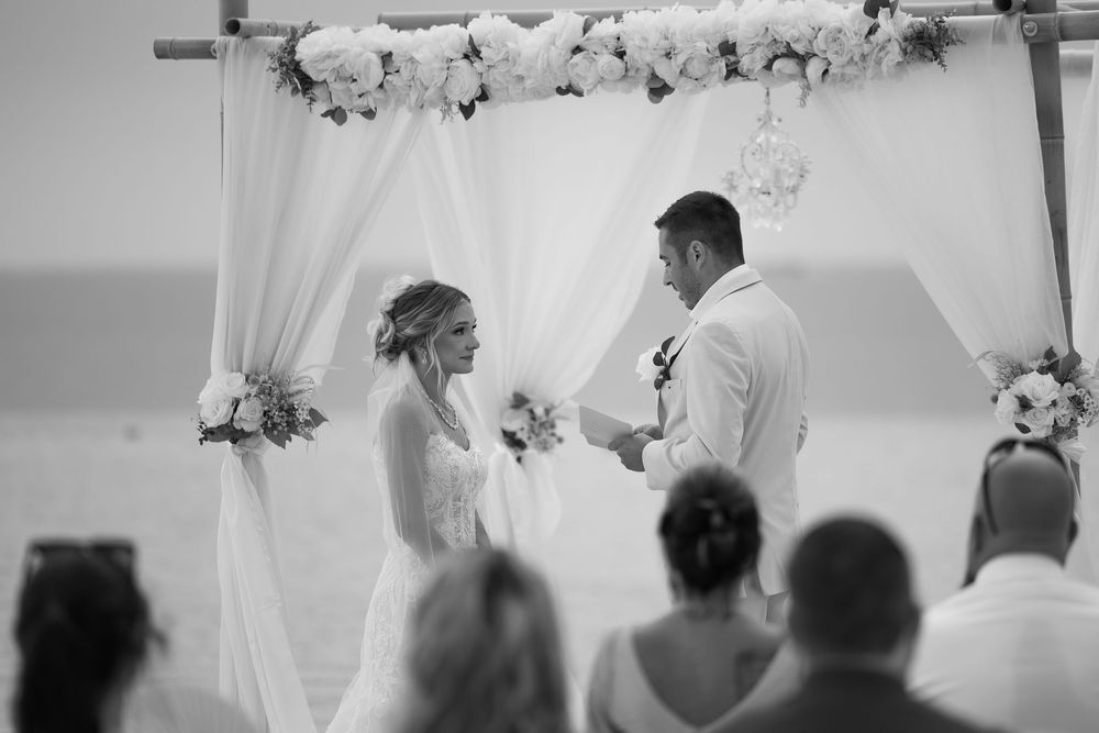 Wedding party members in white and neutral colors stand together in an elegant indoor venue during a celebration.