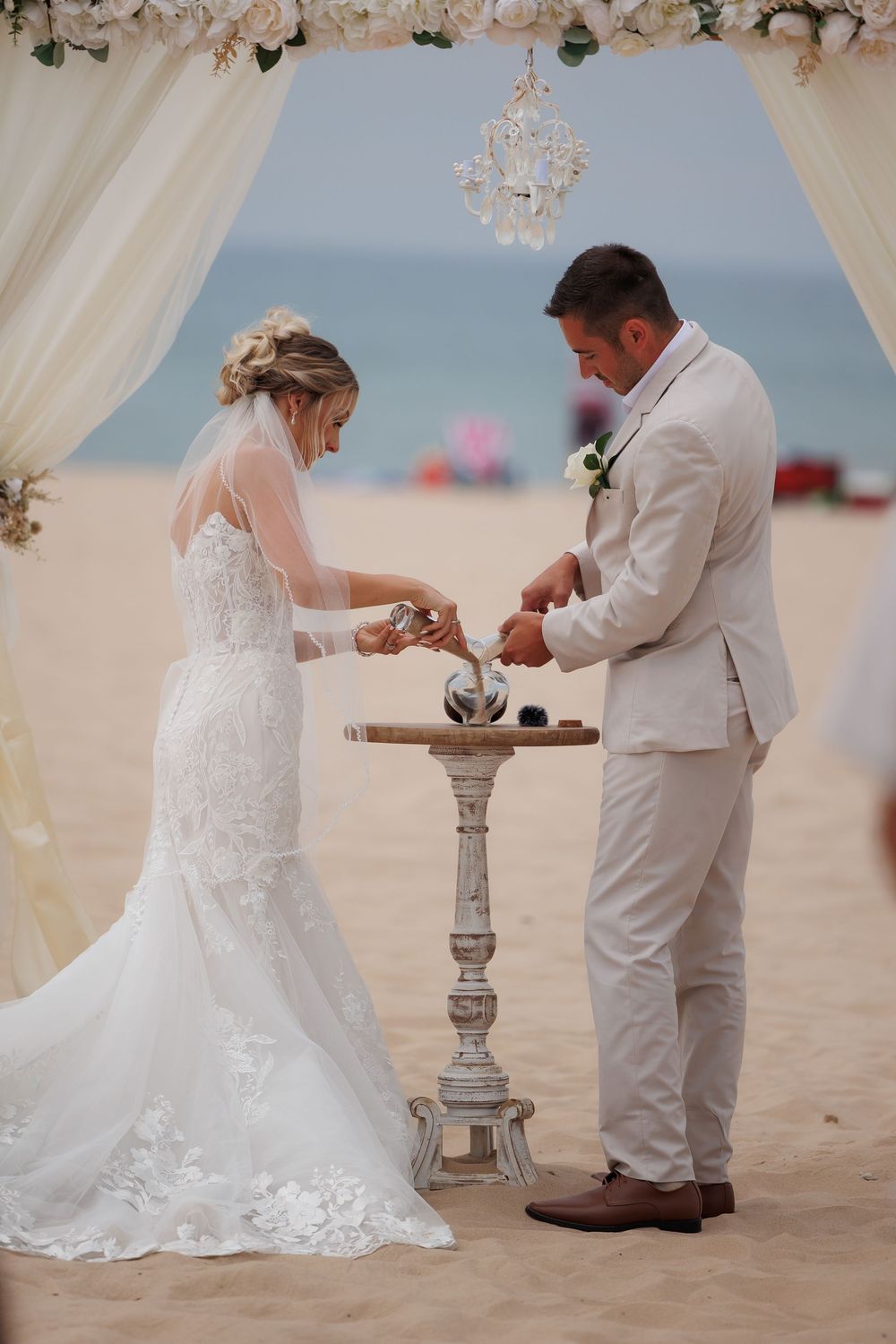 A romantic beach wedding ceremony with a couple exchanging rings under a white draped canopy on sandy shores.