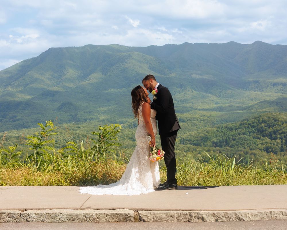 Bride and groom kissing with lush green mountain landscape backdrop on their wedding day.