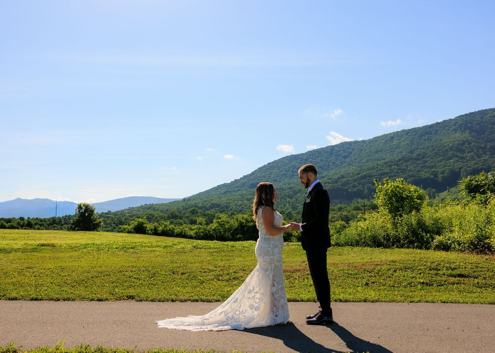 Bride and groom exchange vows on a scenic path with lush green mountains and blue sky backdrop.