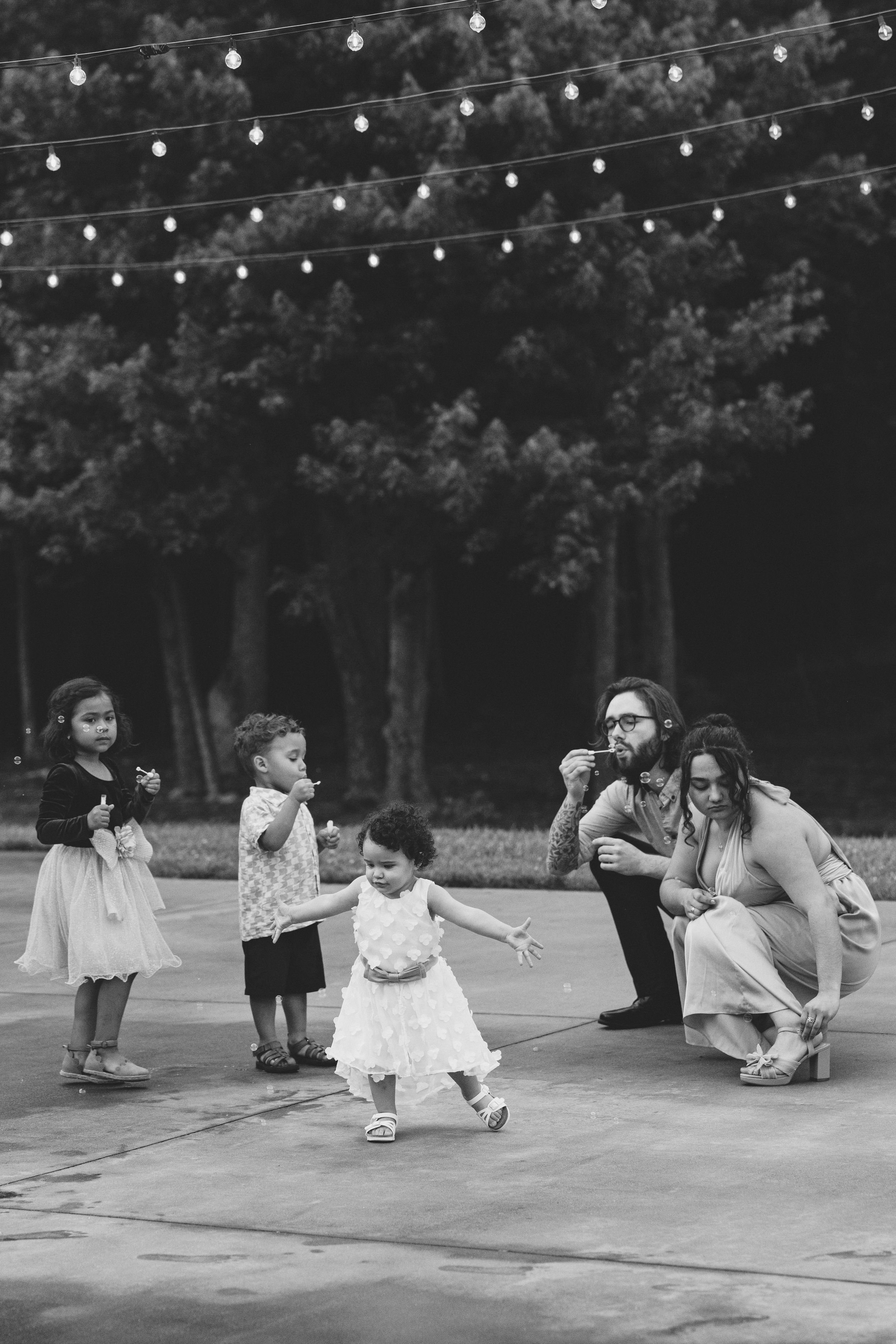 Wedding party members dance and laugh on a patio under string lights at an outdoor reception. Estate and historic venue wedding photographer