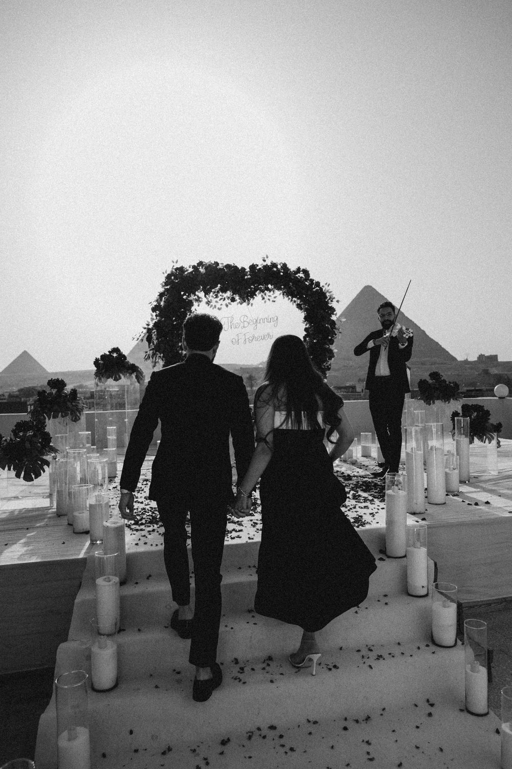 People silhouetted against the sky view the Egyptian pyramids at Giza from a scenic overlook on a hazy day.
