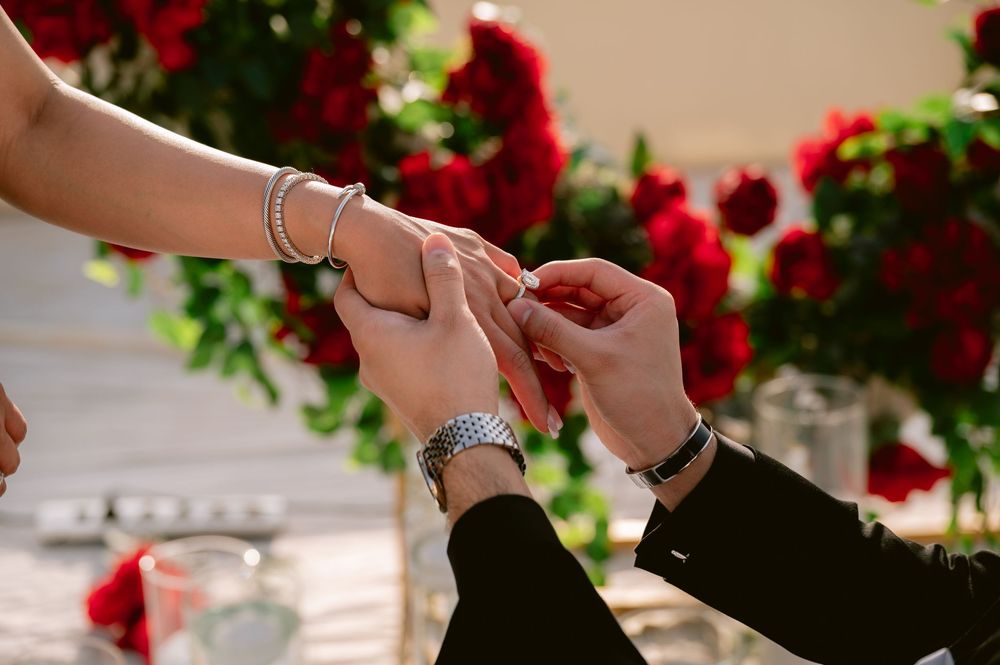 Close-up shot of hands during a proposal moment with red roses in the background.