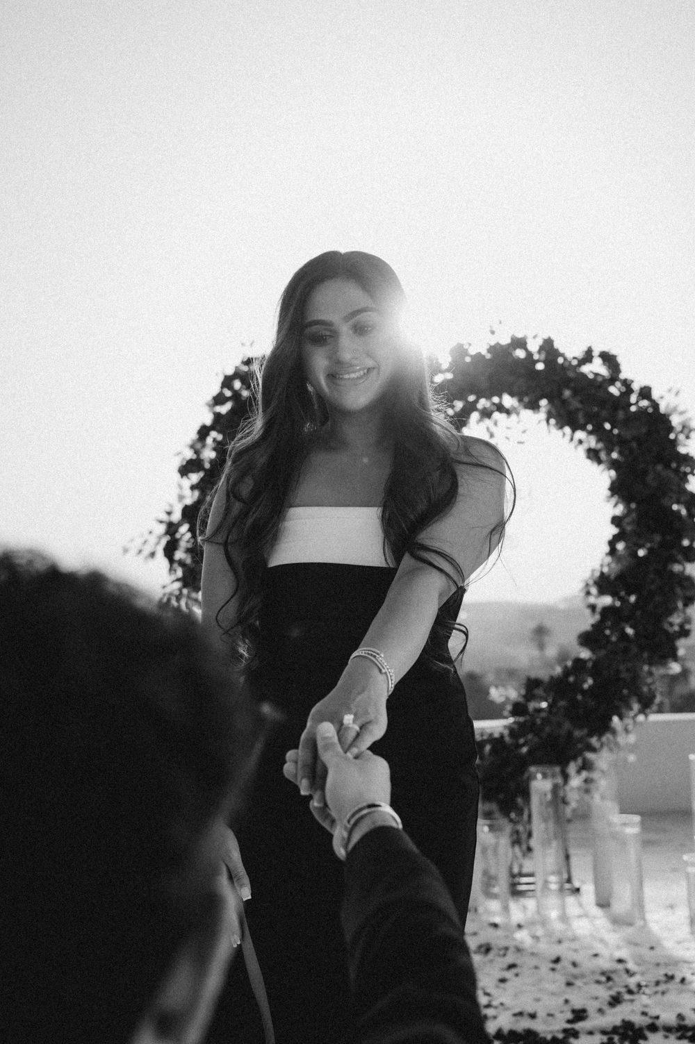A romantic black and white photo sequence showing hands reaching out to connect in front of a sunlit background.