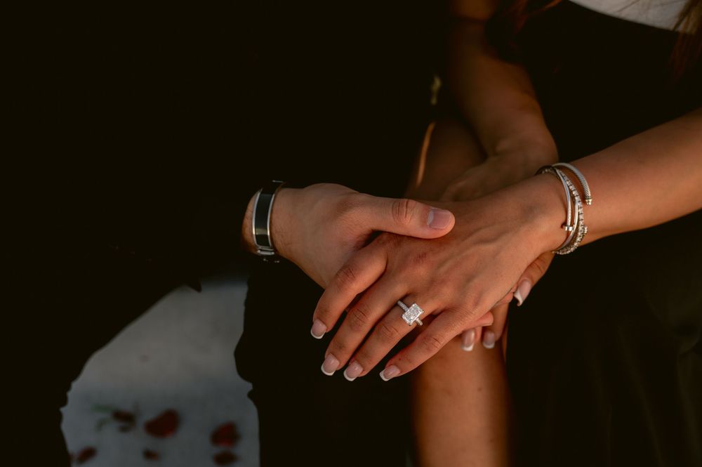 Close-up of intertwined hands showing engagement rings in atmospheric lighting.