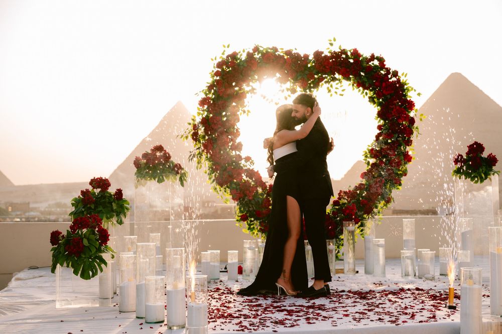 Silhouetted couple shares romantic kiss under floral archway at sunset during beach wedding ceremony.