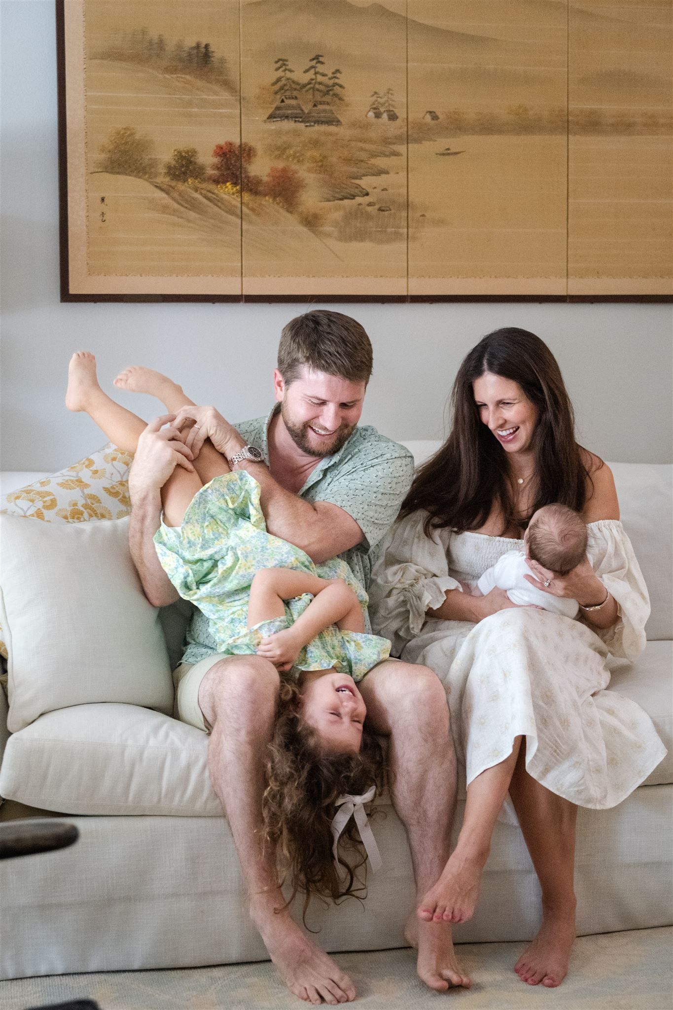 A collection of playful family moments on a white couch shows growing affection and connection in front of an Asian art scroll.