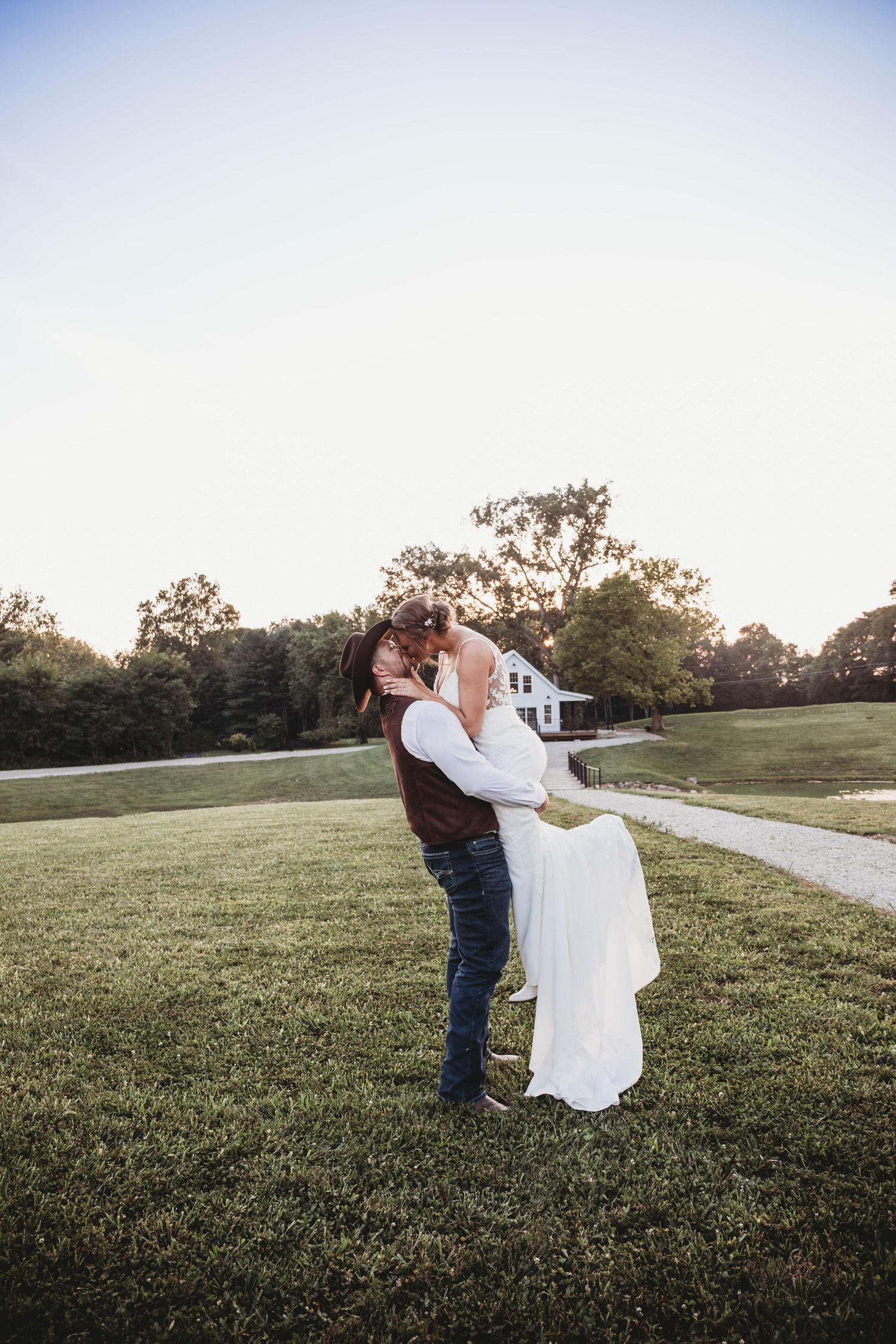 Series of romantically playful dance movements between a couple in a white dress and denim on a grassy hill at sunset.