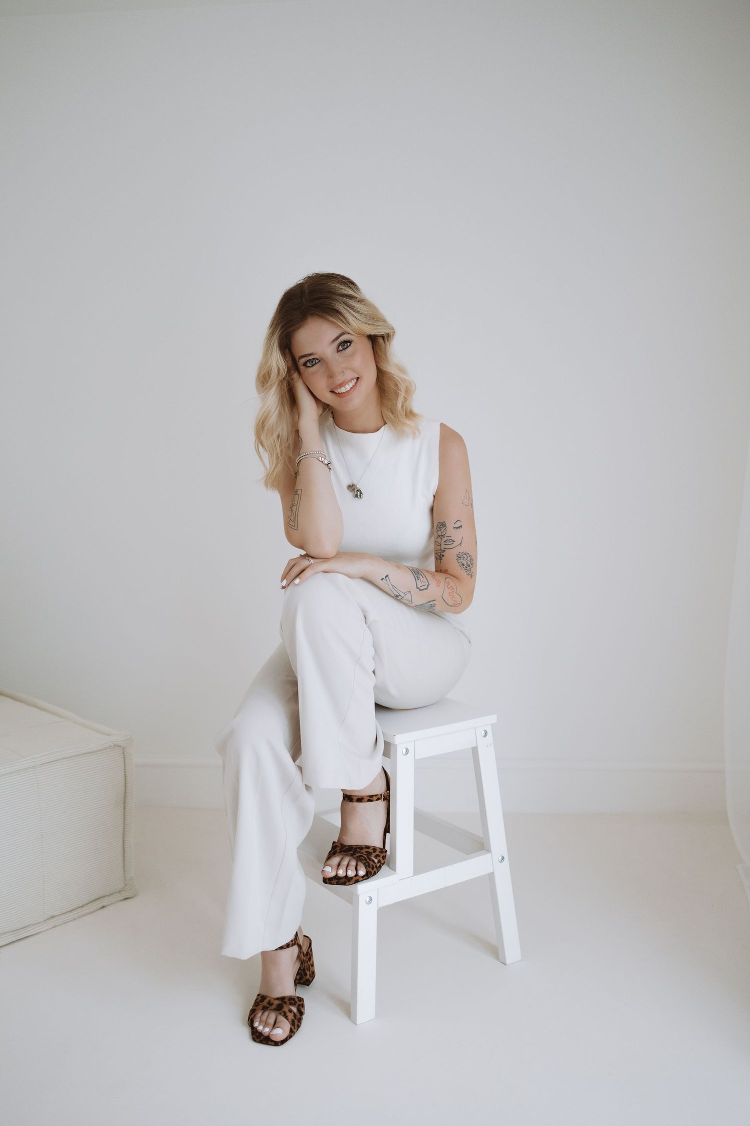 A baby wearing white clothing crawls on a clean white surface in a minimalist setting.