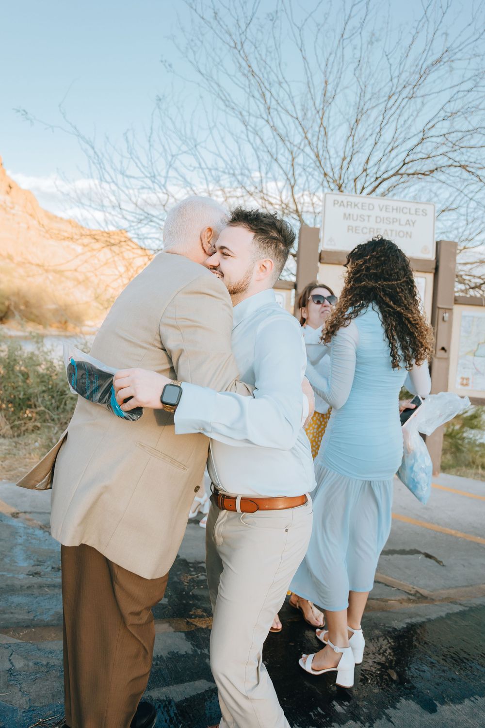Family members embrace in celebration near a mountain trail sign.