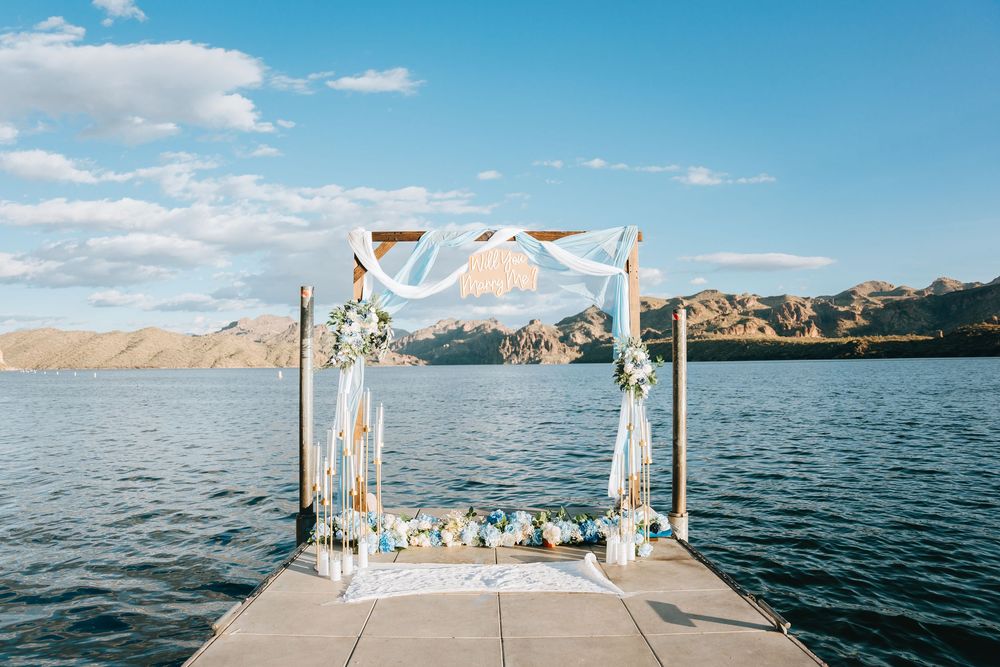 An elegant wedding arch setup on a dock with flowing white fabric and mountain views.