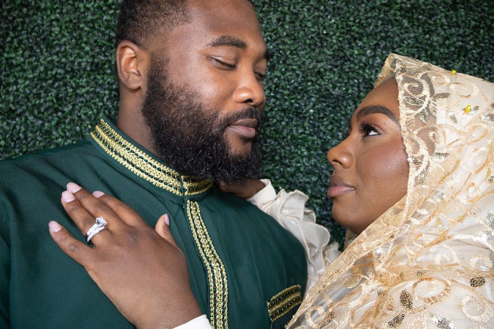 A couple in elegant Islamic wedding attire, man in green and woman in gold hijab, sharing a romantic moment.