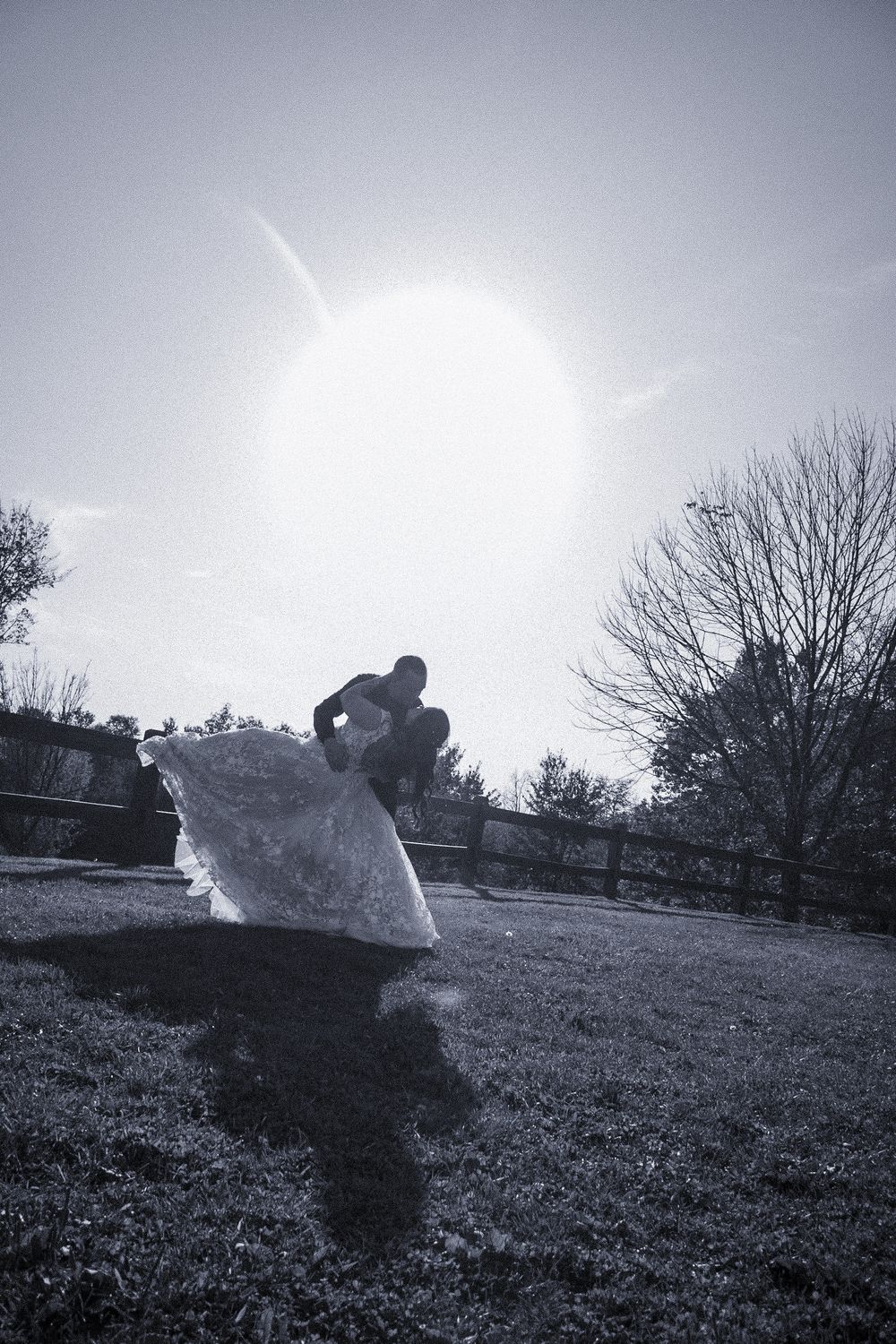 Black and white photo of a person holding a large white fabric outdoors, with bright sun and bare trees in background.