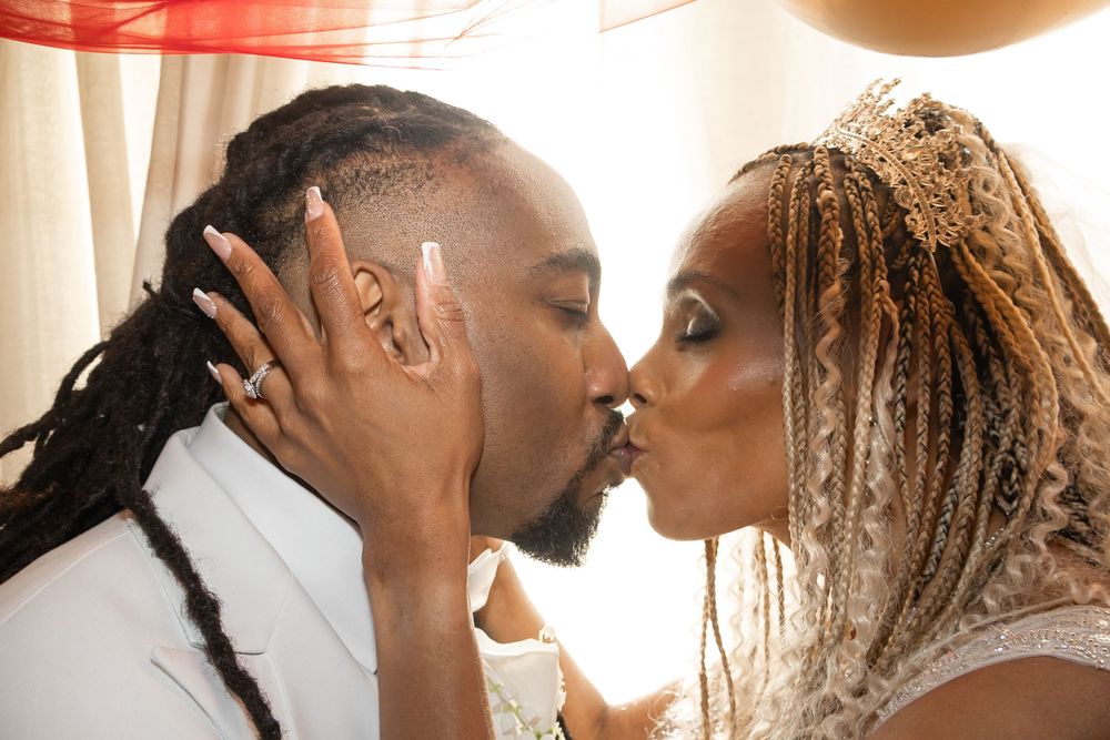 A bride and groom share a romantic kiss on their wedding day, with the bride wearing a crown and braids.