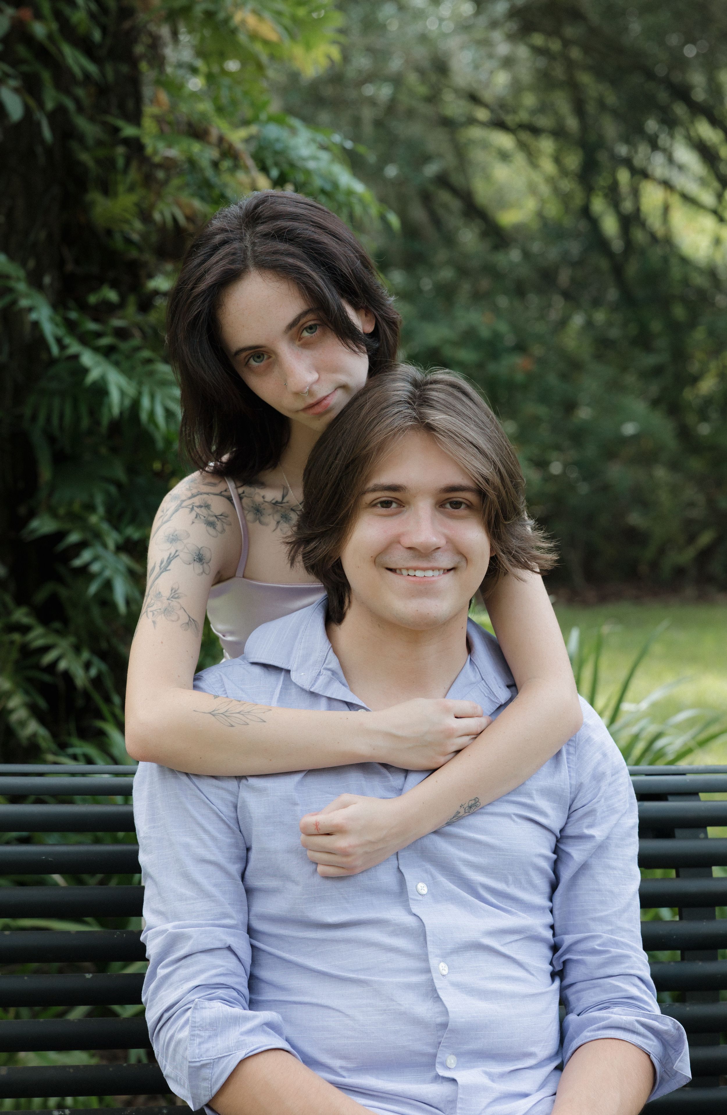 A couple shares an embrace while sitting on a park bench surrounded by greenery.