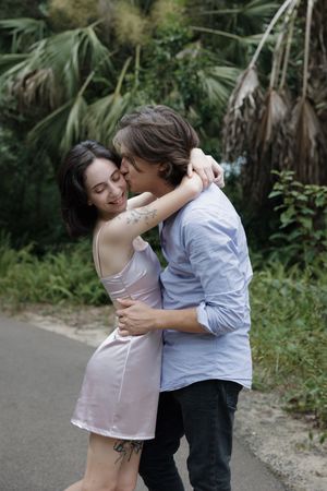 A romantic couple embraces on a palm-lined path, with the person in pink leaning into their partner in blue.
