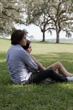 A couple relaxes together on grassy lawn beneath sprawling oak trees.