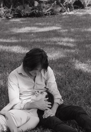 A black and white photograph captures an intimate moment between two people on grass.