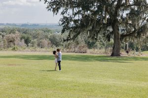 A couple shares a playful moment running across an expansive hilltop lawn.