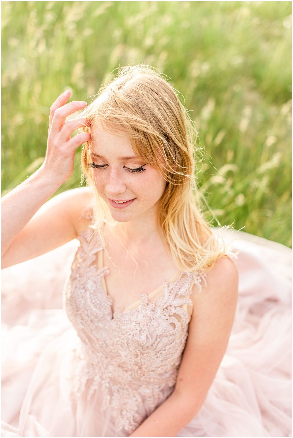 A person in a delicate pink lace dress poses in a sunlit field of tall grass.