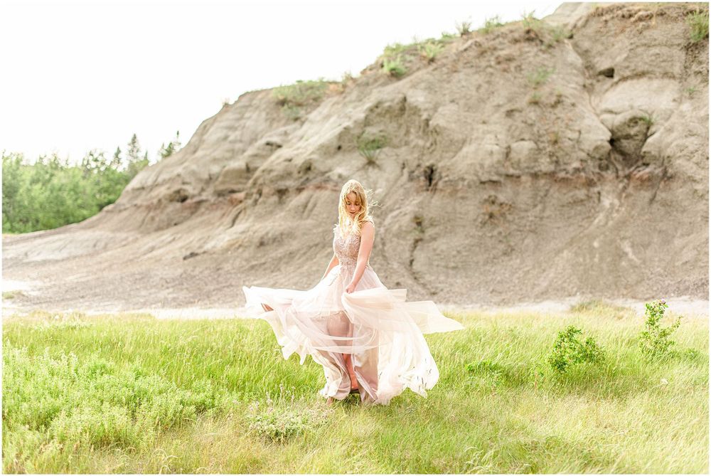 A flowing pink dress twirls gracefully against a natural cliff backdrop in soft sunlight.
