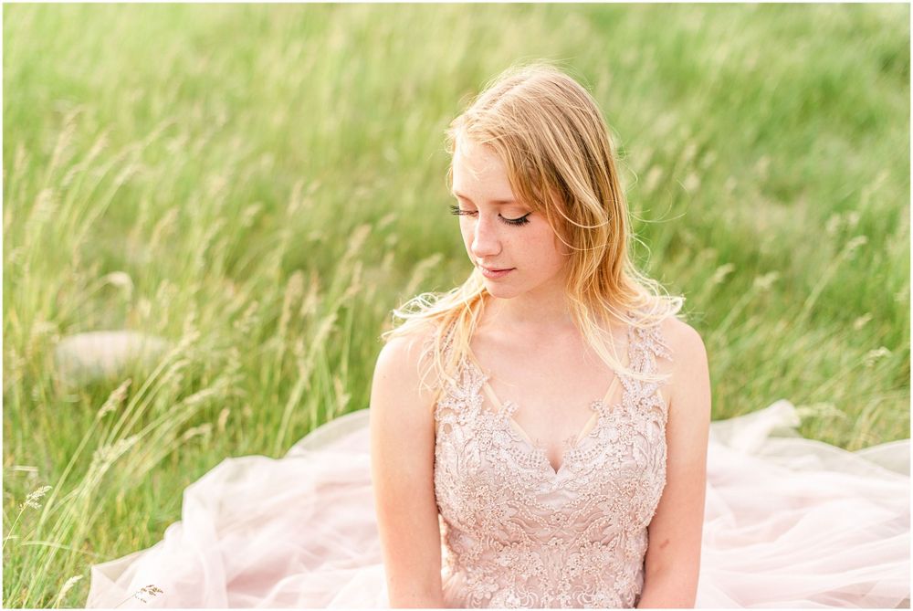 Soft portrait in blush pink lace gown amidst sunlit grassy field.