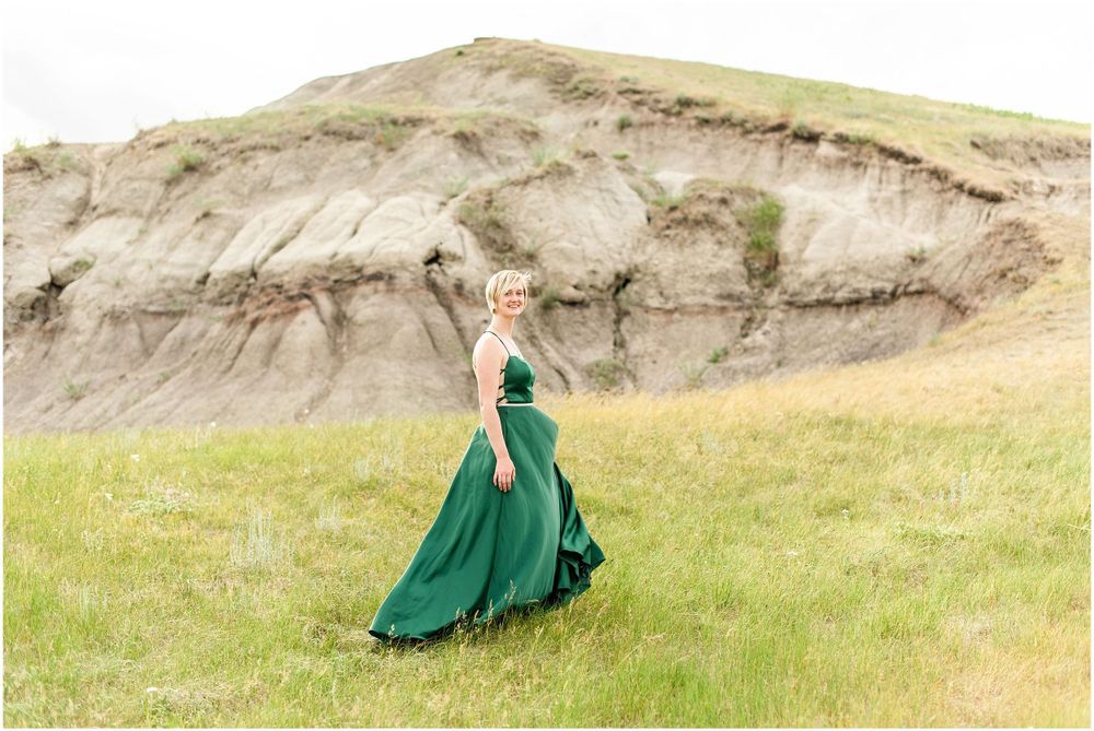 Emerald green ball gown flowing dramatically against rugged cliff landscape.