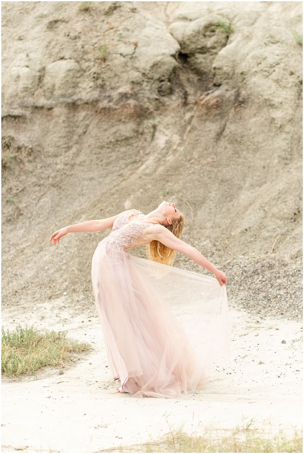 Dancer in flowing pink gown performs graceful movement against rocky cliff backdrop.