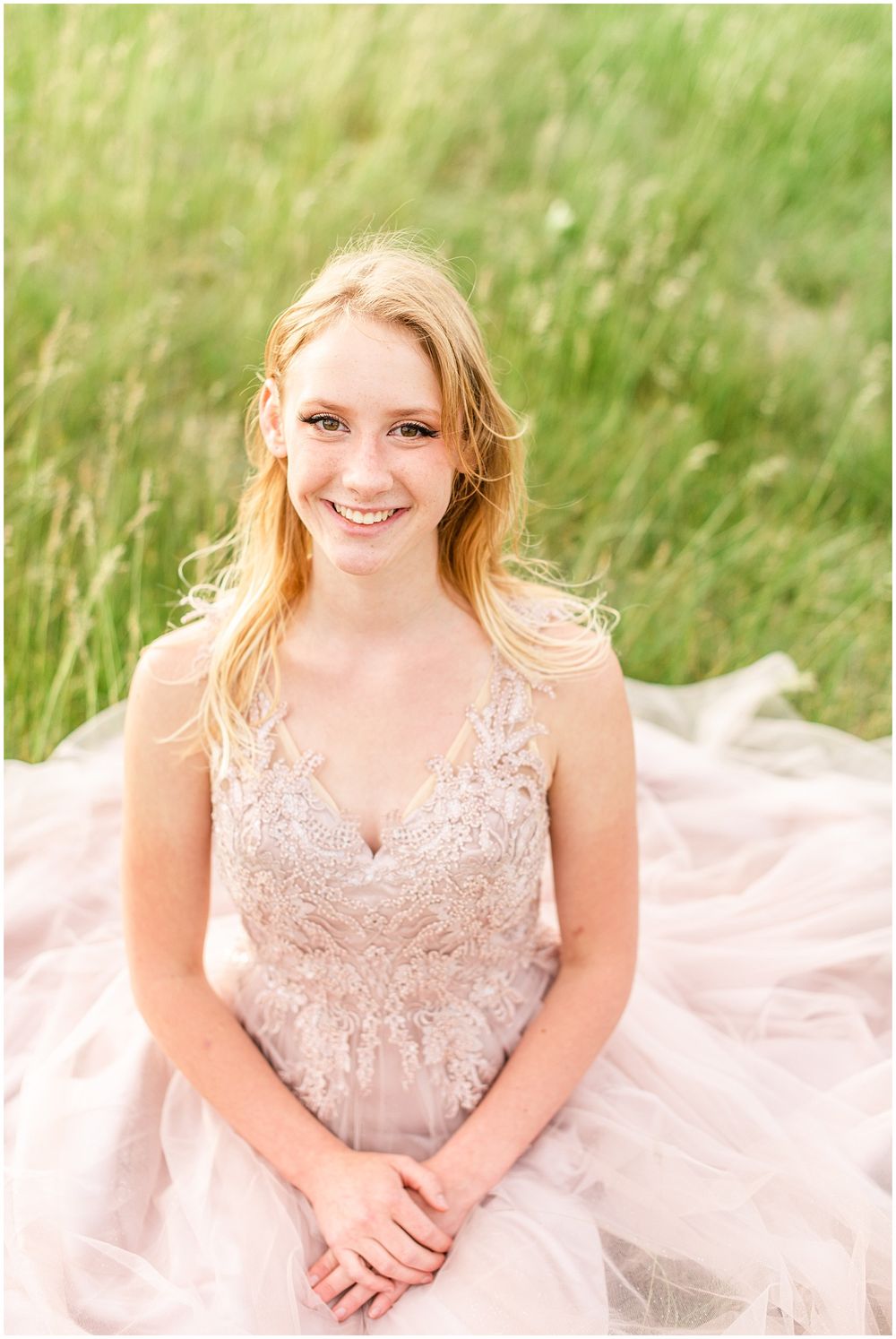Portrait in soft pink lace gown against sunlit grassy background.
