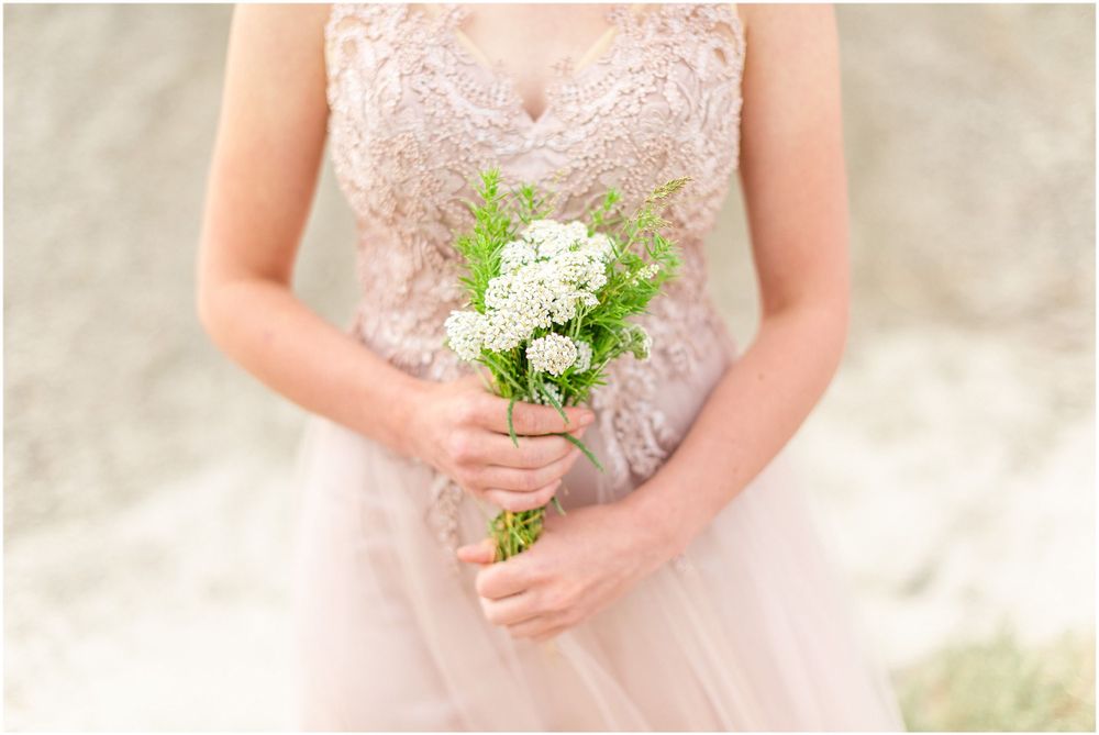 Delicate hands holding a small white wildflower bouquet against a blush pink lace dress.