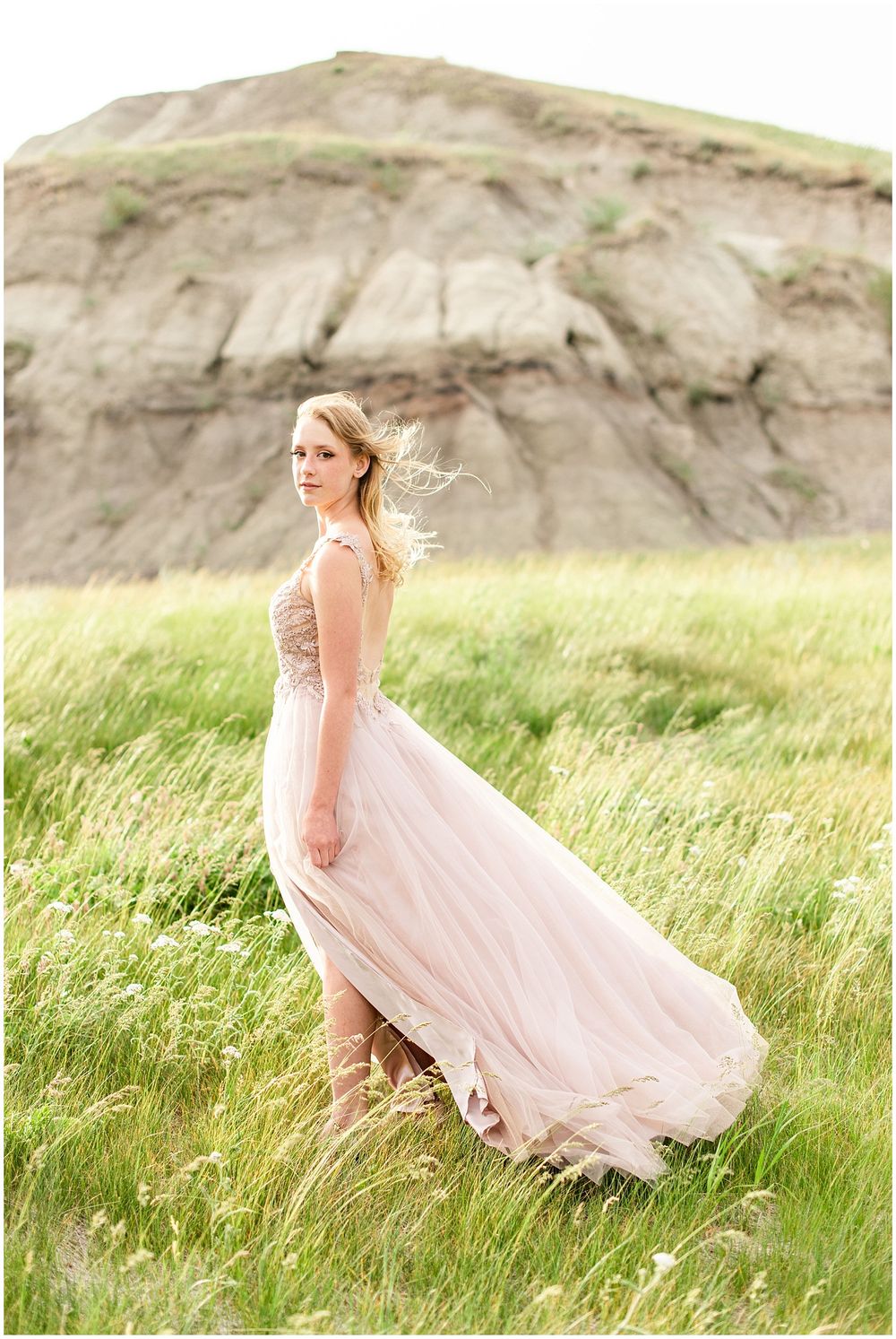 Flowing pink gown catches the breeze on a hillside with dramatic rock formations.
