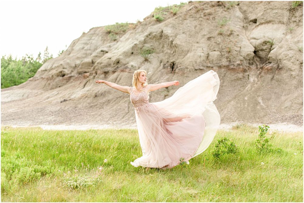 Ethereal pink dress dances in the wind against a backdrop of rugged terrain.
