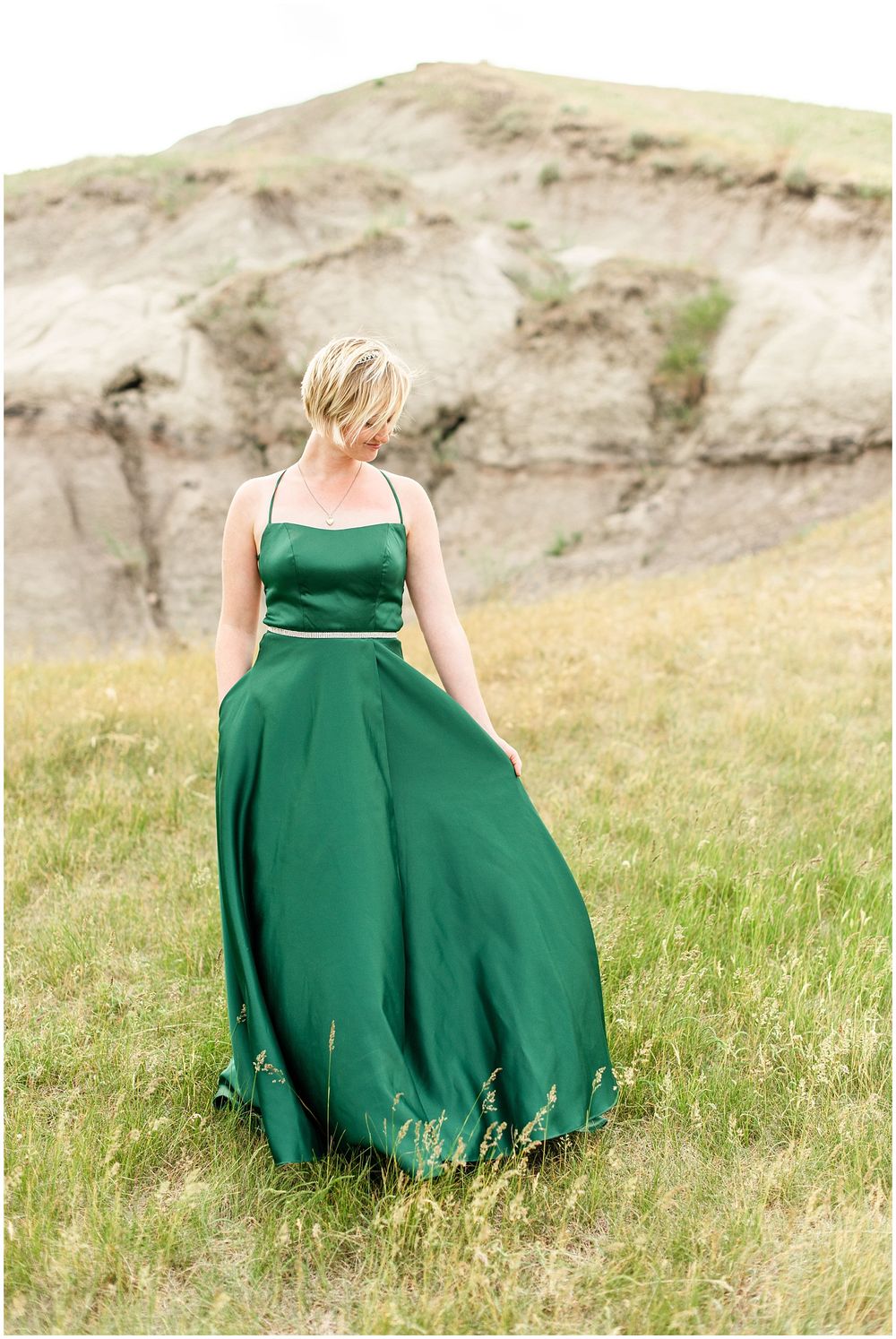 Emerald green formal dress catches wind against rocky hillside landscape.