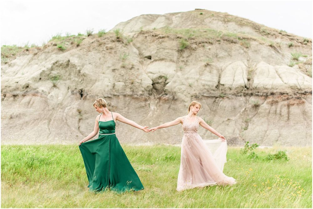Two gowns in pink and green dance together in front of dramatic cliff face.