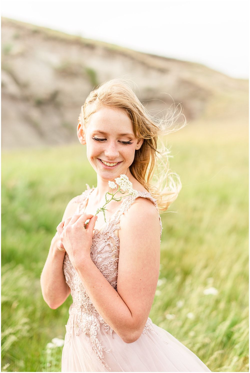 A person in a blush lace gown smiles while standing in a breezy meadow.