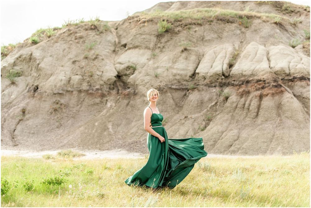 Flowing emerald gown catches wind against dramatic rocky cliff backdrop.