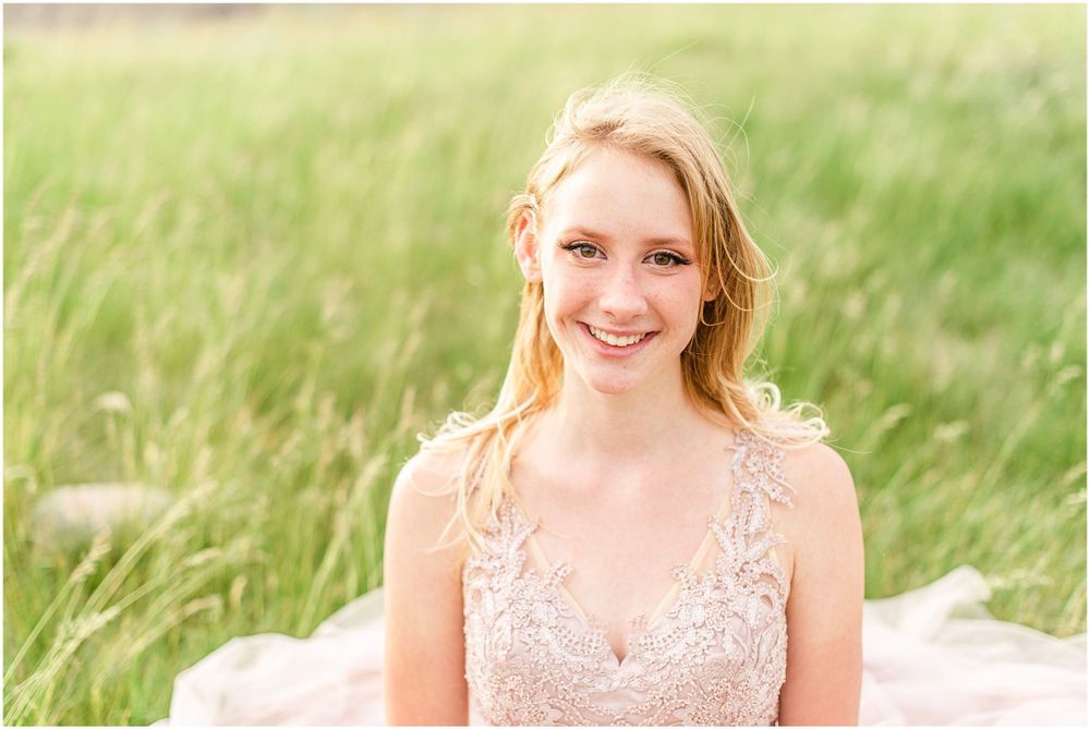 Close up portrait in blush lace gown against sunlit grassy field.