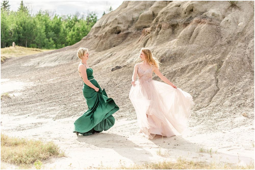Two figures in flowing formal dresses walk through rocky terrain.