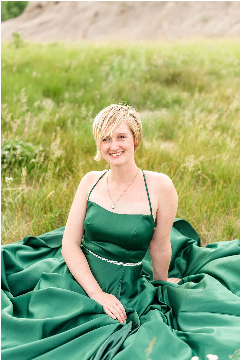 Portrait in emerald satin gown sitting in sunlit meadow.