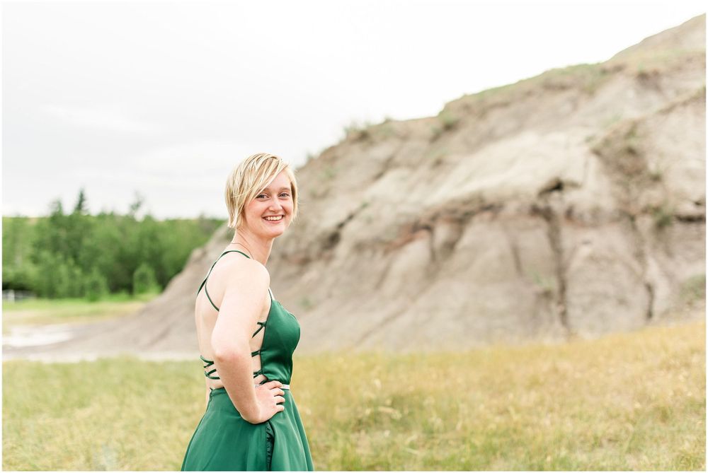 A figure in an emerald green dress poses in front of weathered cliffs and grassland.