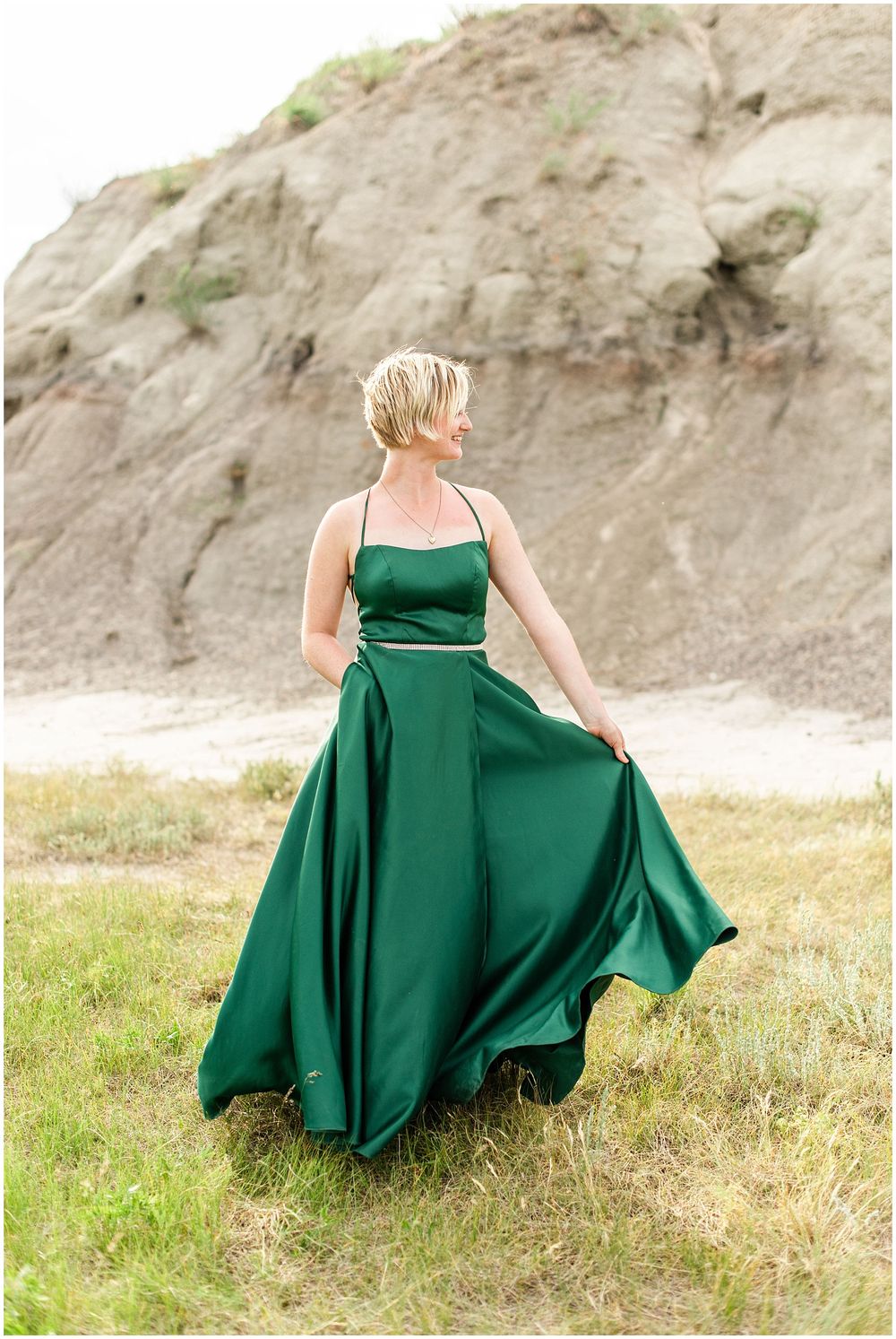 An elegant emerald satin gown billows in the wind against rugged cliff scenery.